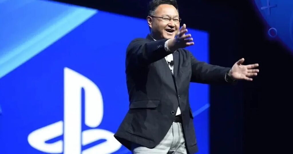 Shuhei Yoshida davanti a console moderne con grafico dei costi in salita sullo sfondo