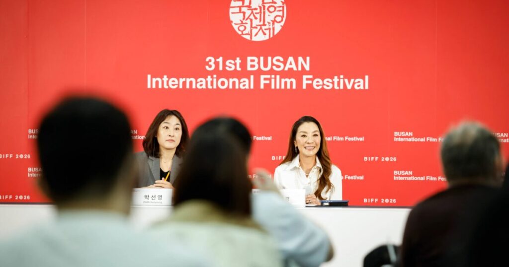 Michelle Yeoh sul palco di un festival internazionale con sfondo rosso e microfono