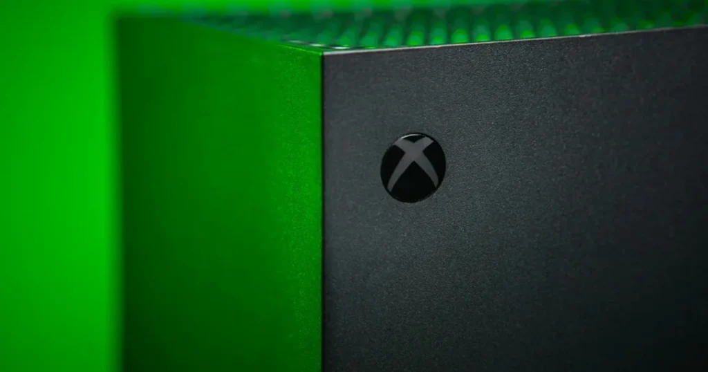 Asha Sharma davanti al logo Xbox con grafica che richiama riorganizzazione aziendale